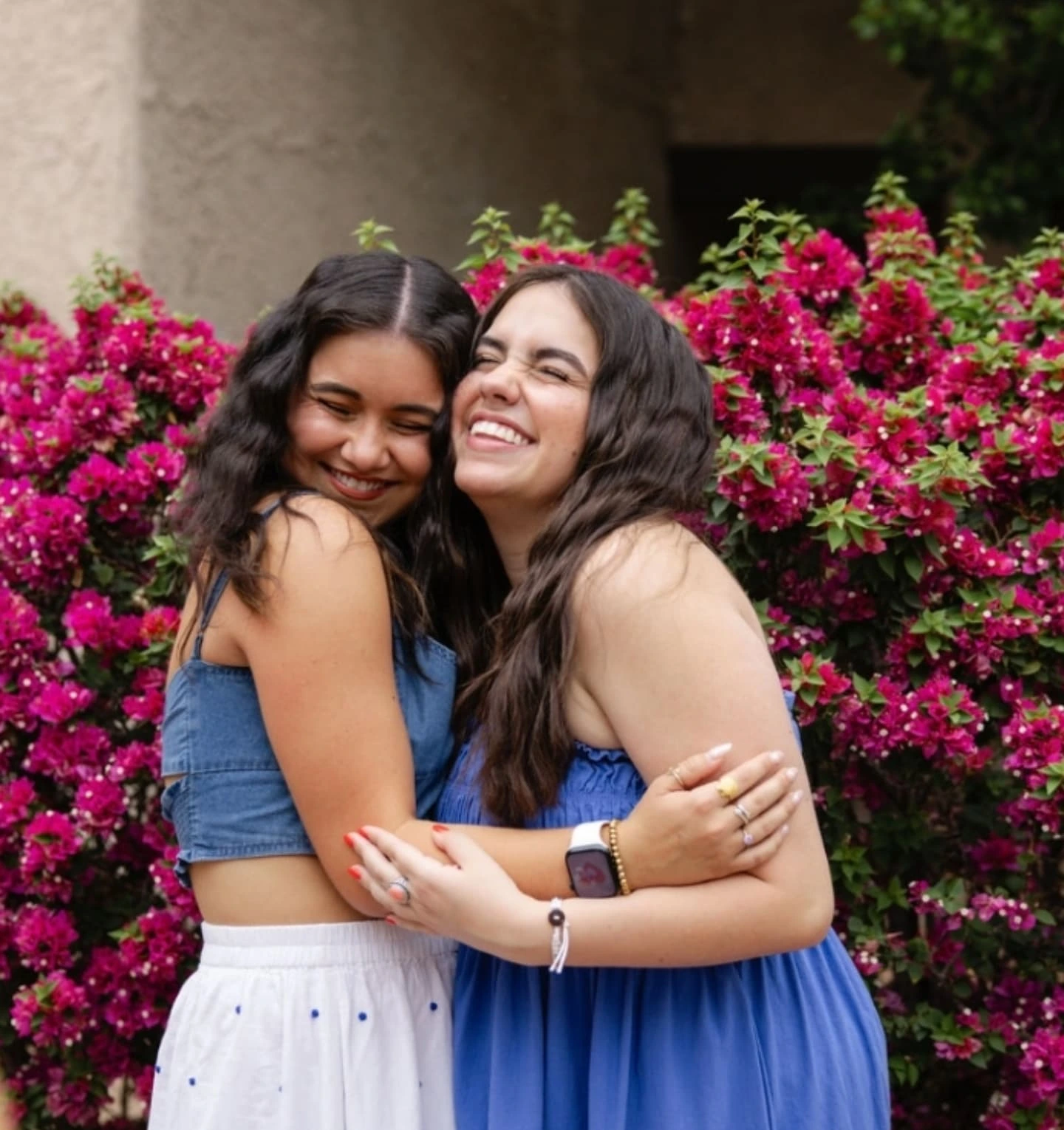 Two women hugging in front of bright pink flowers