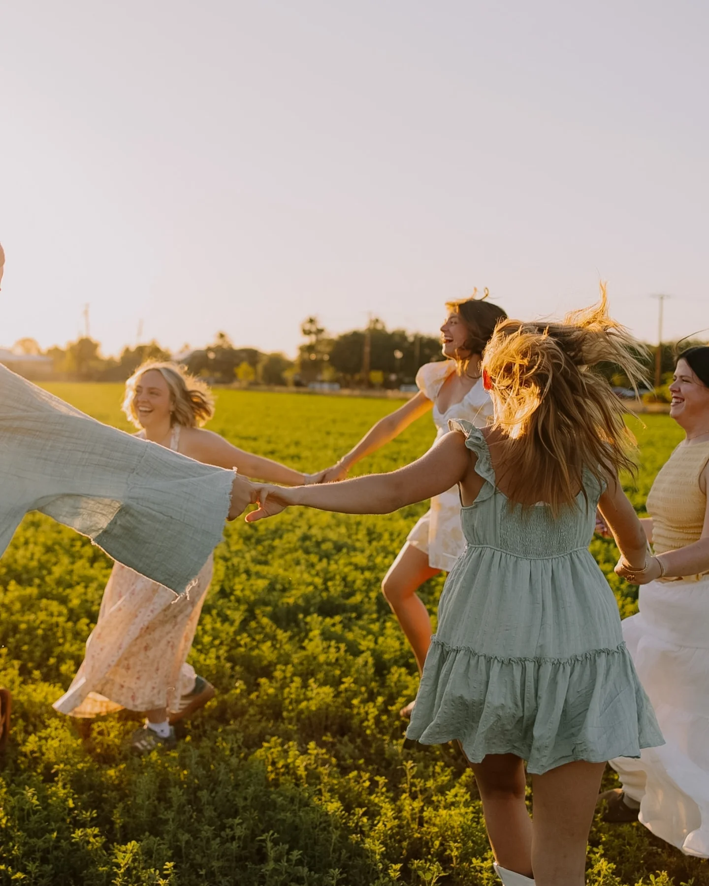 Women holding hands and running together through a field at sunset